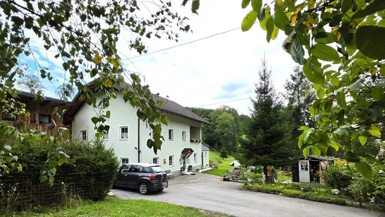 Landhaus mit heller Fassade, umgeben von Bäumen und einem gepflegten Vorgarten mit Zufahrt.