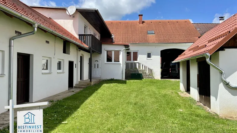 Blick auf den Innenhof der Immobilie mit mehreren Gebäuden und grünem Rasen unter blauem Himmel.
