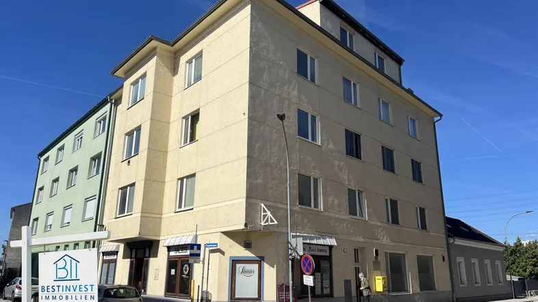 Mehrstöckiges Wohn- und Geschäftshaus mit gelber Fassade an einer Straßenecke unter blauem Himmel.