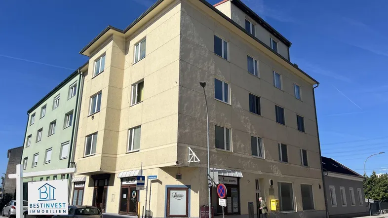 Mehrstöckiges Eckgebäude mit hellgelber Fassade und Geschäftsflächen im Erdgeschoss an einem sonnigen Tag.