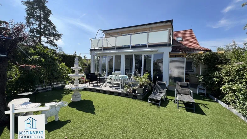 Großzügiger Gartenbereich mit Kunstrasen, Springbrunnen und einer möblierten Terrasse am Haus.