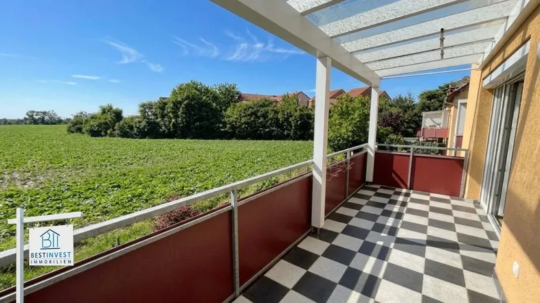 Geräumiger Balkon mit Schachbrettmuster-Fliesen und weitem Blick über grüne Felder.