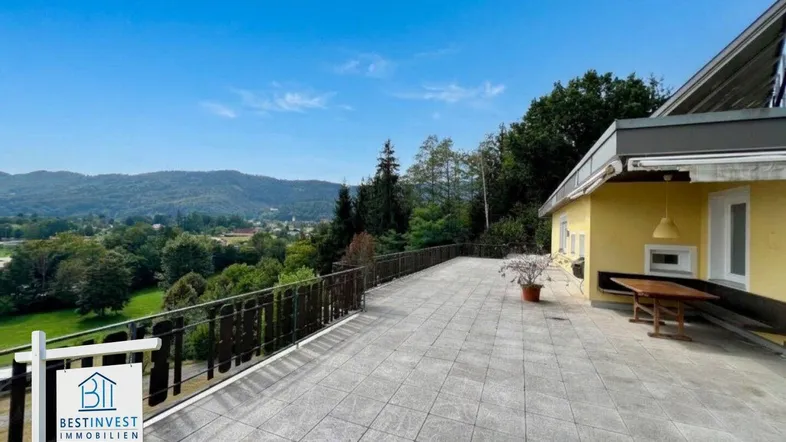 Große geflieste Terrasse mit Holzzaun und weitem Blick über die Landschaft und Berge.