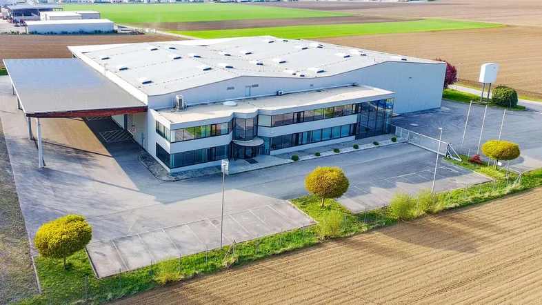 Luftaufnahme eines modernen Industrie- und Bürogebäudes mit weitläufigen Parkflächen und angrenzenden Feldern.