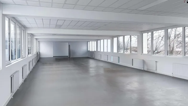 Großer, leerer Büroraum mit vielen Fenstern, die viel natürliches Licht hereinlassen.