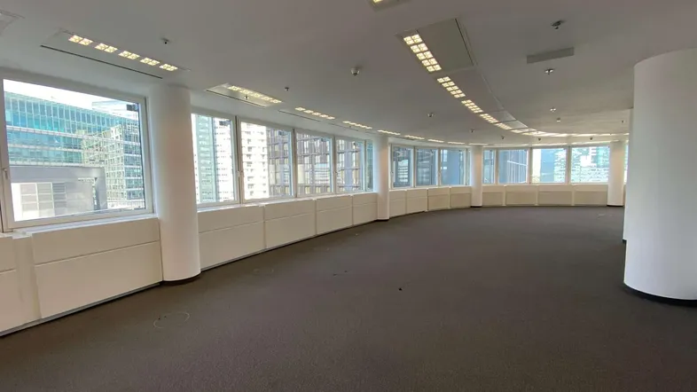 Großer, offener Büroraum mit Teppichboden und einer langen Reihe von Fenstern, die viel Tageslicht hereinlassen.