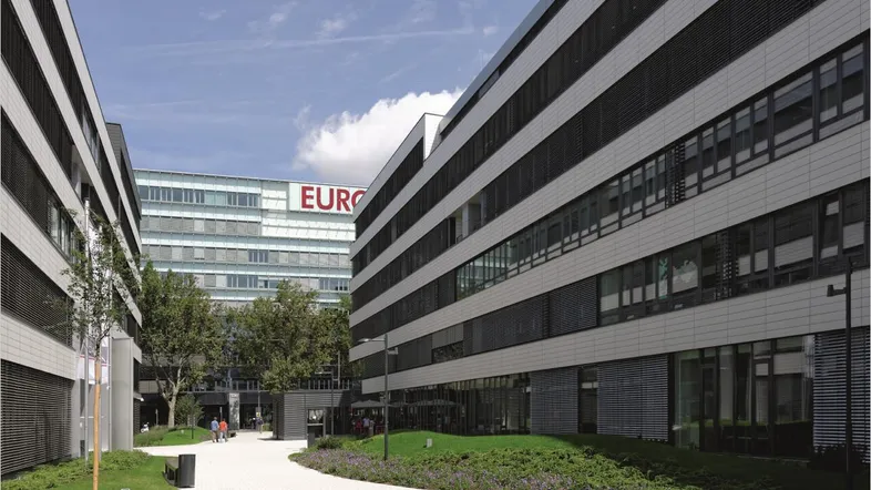 Moderne Bürogebäude mit heller Fassade und gepflegtem Außenbereich unter blauem Himmel.