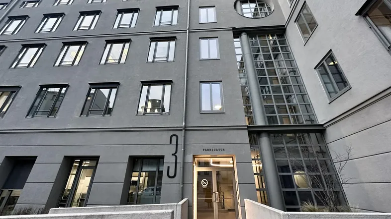 Modernes Bürogebäude mit grauer Fassade und großen Fenstern, das einen professionellen Eindruck vermittelt.