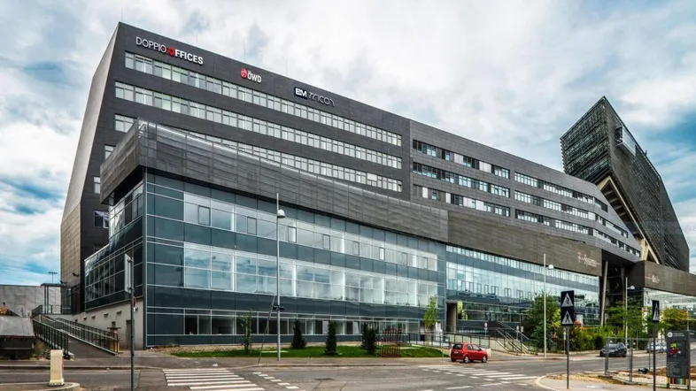 Großes, modernes Bürogebäude mit Glasfassade und Firmenlogos an der Außenseite.