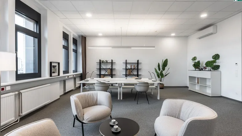Helles und modernes Büro mit Teppichboden, großen Fenstern, Klimaanlage und verschiedenen Arbeitsbereichen.