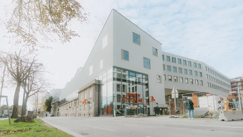 Modernes Gebäude mit markanter Architektur, Glasfassade im Erdgeschoss und umliegender Straße mit Bäumen.