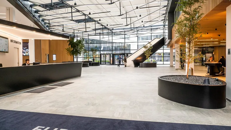 Großzügige, moderne Bürolobby mit hoher Glasdecke, hellem Boden und Empfangsbereich.