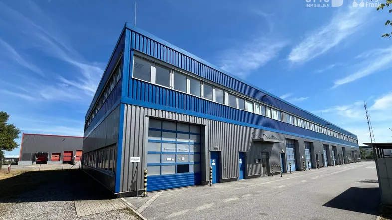 Modernes Industriegebäude mit blauer Fassadenverkleidung und mehreren Rolltoren unter blauem Himmel.