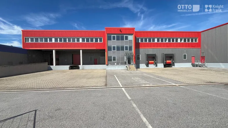Moderne Gewerbeimmobilie mit roter Fassade, Laderampen und Bürobereich unter blauem Himmel.