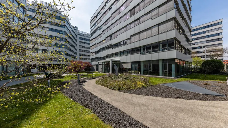 Moderne Bürogebäude mit gepflegtem Innenhof und Grünflächen unter blauem Himmel.