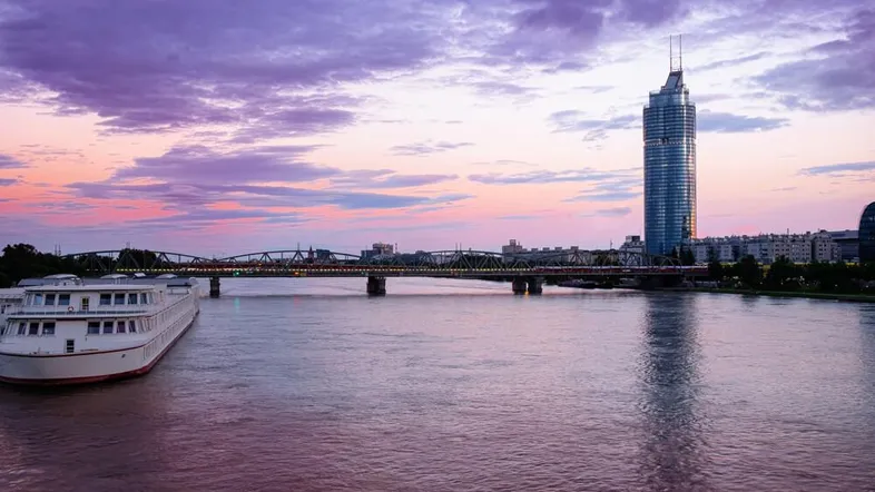 Abenddämmerung über der Donau mit beleuchteter Brücke und markantem Hochhaus am Ufer.