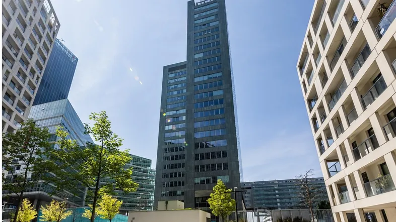Blick auf ein modernes Hochhaus mit Glasfassade und umliegenden Gebäuden in einer städtischen Umgebung.