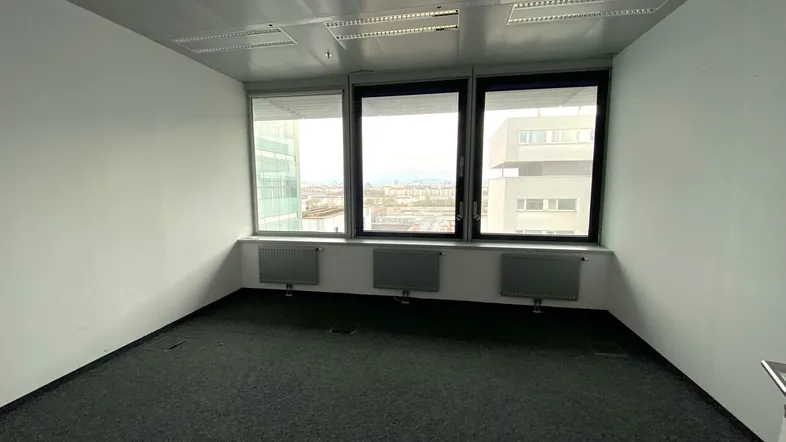 Leeres Büro mit Teppichboden, großen Fenstern und Heizkörpern unterhalb der Fenster.