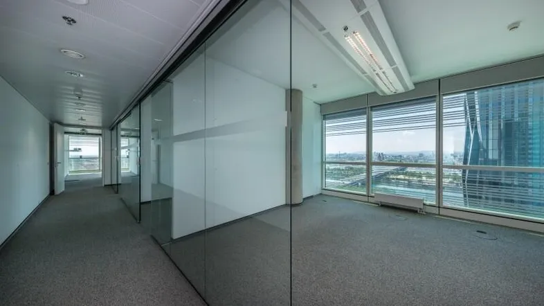 Moderner Bürogang mit Glaswänden und einem hellen Büroraum mit weitem Stadtblick.