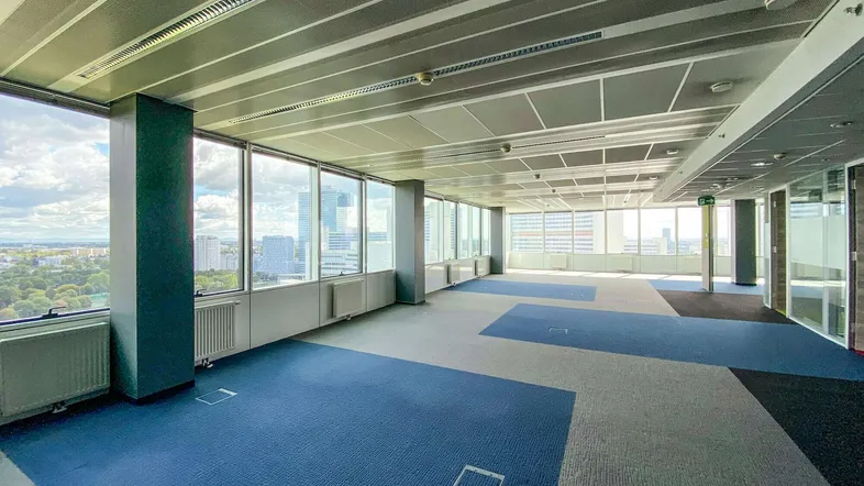 Geräumiges, leeres Büro mit großen Fenstern, die einen weiten Blick auf die Stadt bieten und modularem Teppichboden.