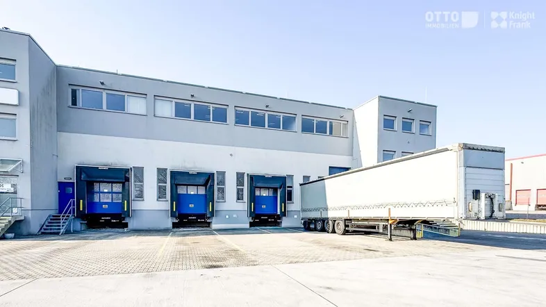 Außenansicht eines modernen Logistikzentrums mit mehreren Laderampen und einem abgestellten LKW-Anhänger.
