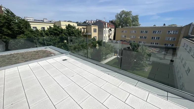Eine moderne Dachterrasse mit Glasgeländer und Blick auf umliegende Gebäude und Grünflächen.
