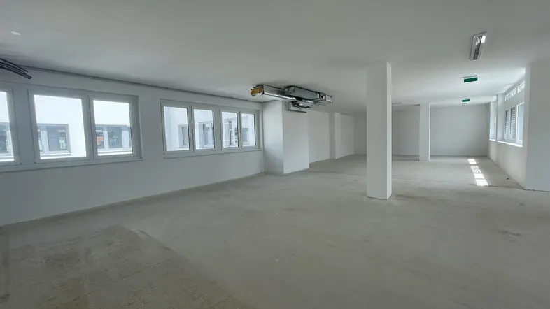 Geräumiger, unmöblierter Büroraum mit vielen Fenstern und Betonboden, bereit für den Ausbau.