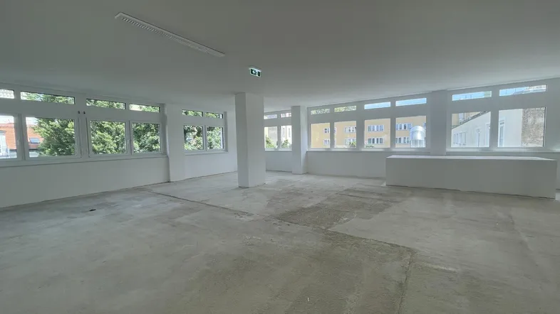 Geräumiger, heller Büroraum mit vielen Fenstern und Rohbetonboden, bereit für den Ausbau.