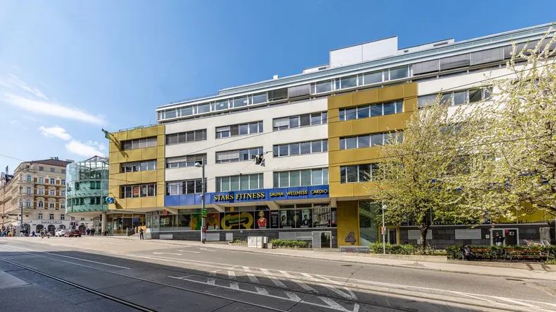Gebäudeansicht eines modernen Geschäftshauses mit gelben und weißen Fassadenelementen an einer belebten Straße.