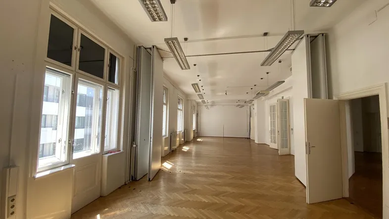 Großes, leeres Büro mit Fischgrätparkett, hohen Fenstern und Deckenleuchten, bereit zur Nutzung.