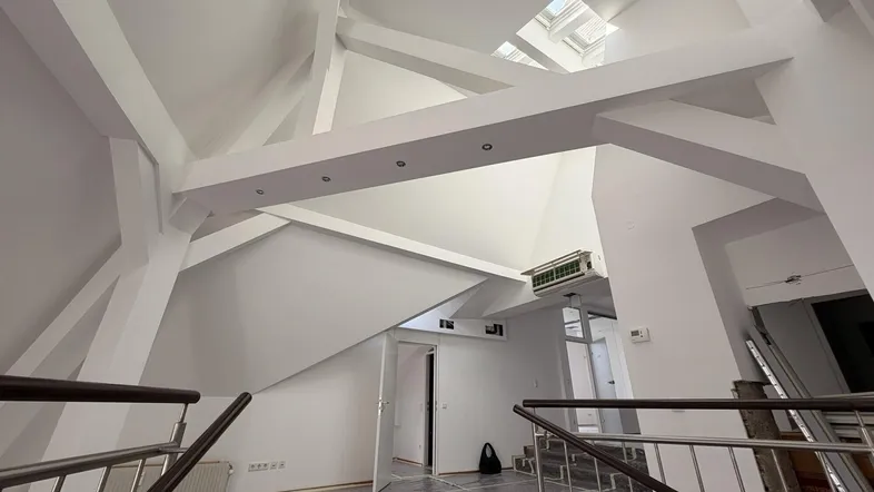 Geräumiger Innenraum mit hohen, gewölbten Decken, sichtbaren Holzbalken und Oberlichtern, der sich in Renovierung befindet.