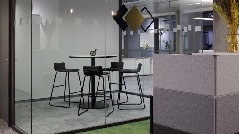 Moderner Besprechungsbereich in einem Büro mit Glastrennwänden und hohen Barhockern.