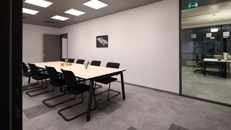 Moderner Konferenzraum mit großem Tisch, bequemen Stühlen und Teppichboden in Grautönen.