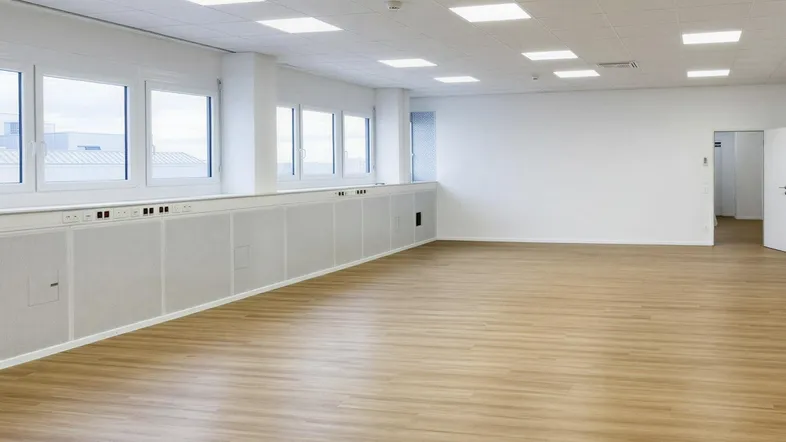 Geräumiges, helles Büro mit vielen Fenstern und modernem Laminatboden, ideal für flexible Arbeitsplatzgestaltung.