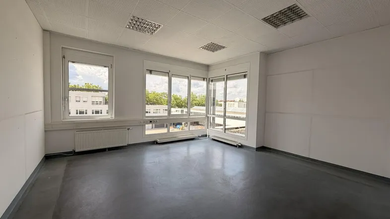 Geräumiges Büro mit großen Fenstern, die viel Tageslicht hereinlassen und einen Blick nach draußen bieten.