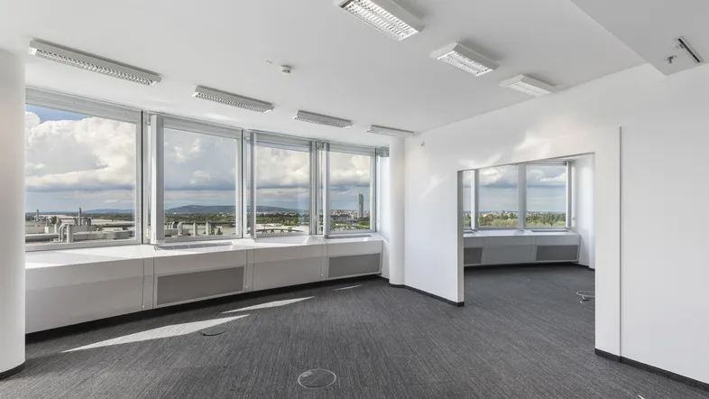 Geräumiges, leeres Büro mit großen Fenstern und Blick auf die Stadtlandschaft.