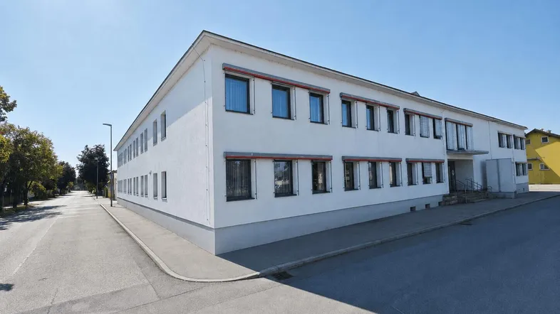 Großes, weißes Geschäftsgebäude mit vielen Fenstern und Jalousien an einem sonnigen Tag.