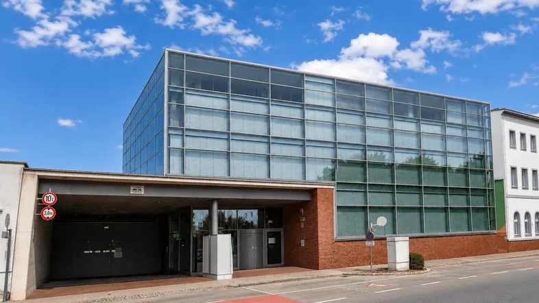 Modernes Bürogebäude mit Glasfassade und integrierter Tiefgarageneinfahrt an einer städtischen Straße.