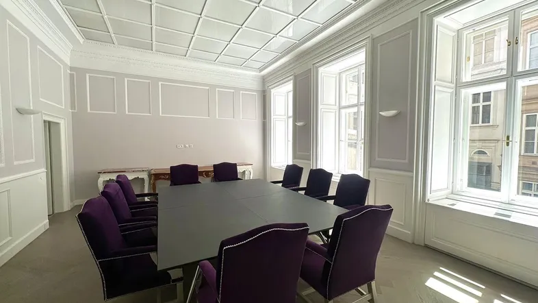 Eleganter Konferenzraum mit großen Fenstern, Kassettendecke und lila Stühlen in einem klassischen Ambiente.