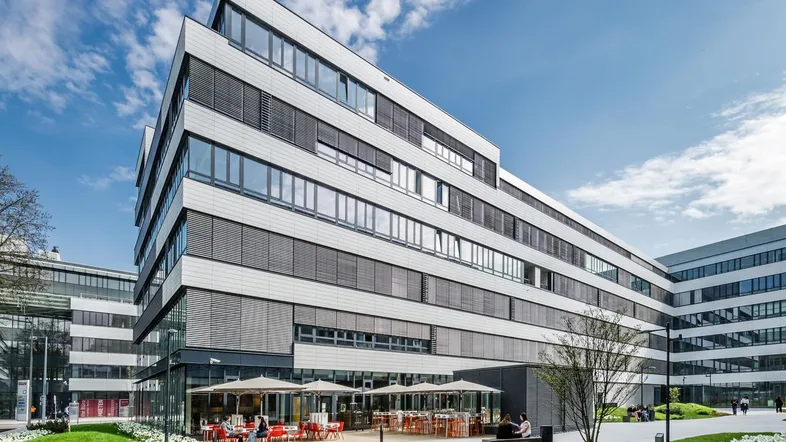 Modernes Bürogebäude mit einer einladenden Außenterrasse, umgeben von gepflegten Grünflächen und Blumen.
