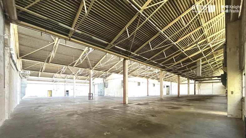 Geräumige, leere Lagerhalle mit hoher Decke, sichtbaren Metallträgern und Betonboden.