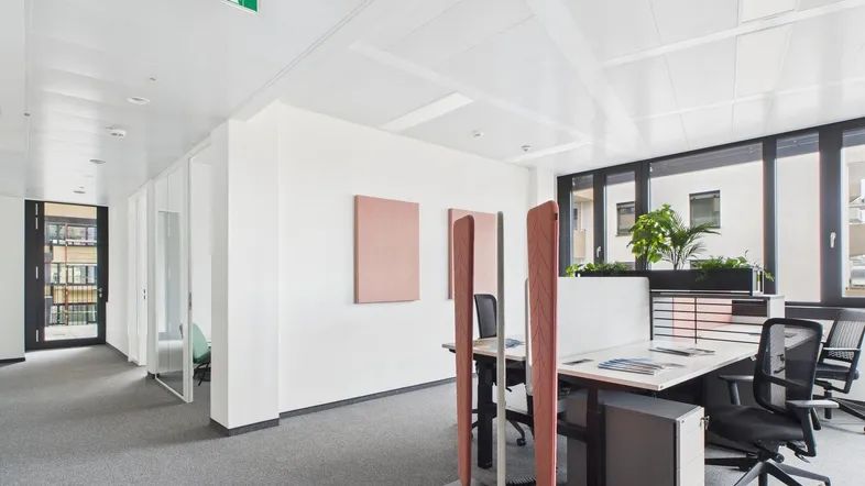 Moderner Großraumbüro mit ergonomischen Arbeitsplätzen, Teppichboden und großen Fenstern für viel Tageslicht.