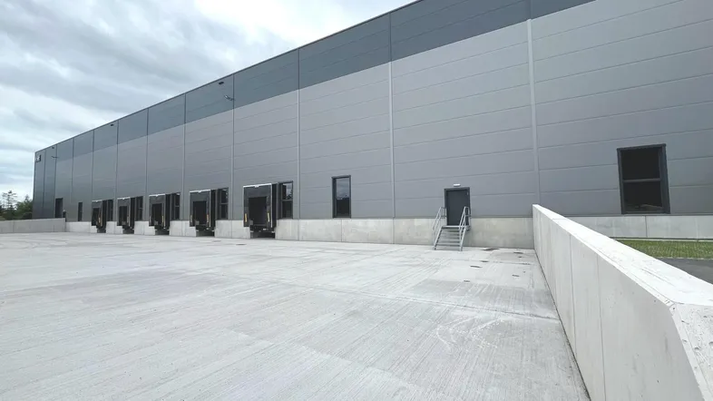 Ansicht der modernen Lagerhalle mit Laderampen, einem Außentreppenaufgang und weitläufiger Betonfläche.