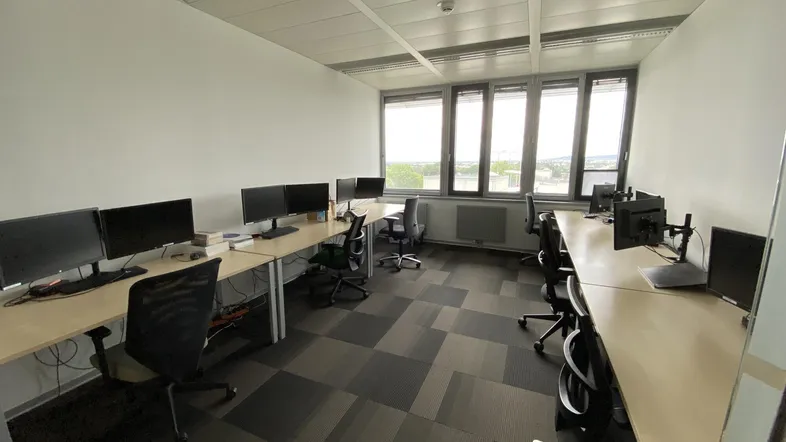 Geräumiges Büro mit mehreren Arbeitsplätzen, großen Fenstern und Teppichfliesen in modernem Design.