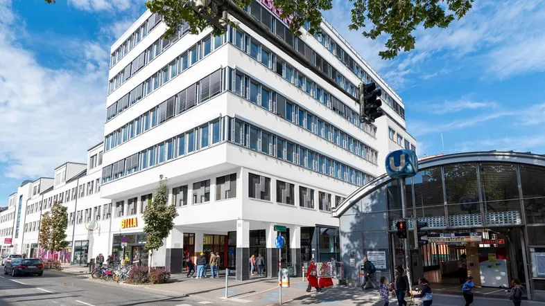 Modernes Bürogebäude an einer belebten Straße mit U-Bahn-Station und Geschäften im Erdgeschoss.