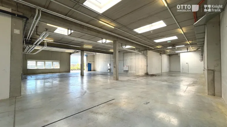 Geräumige Lagerhalle mit hohen Decken, Betonboden und Oberlichtern, ideal für industrielle Nutzung.