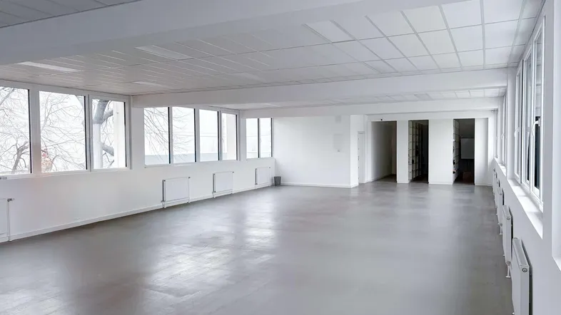 Geräumiger, leerer Gewerberaum mit durchgehenden Fensterfronten und Zugang zu weiteren Bereichen.