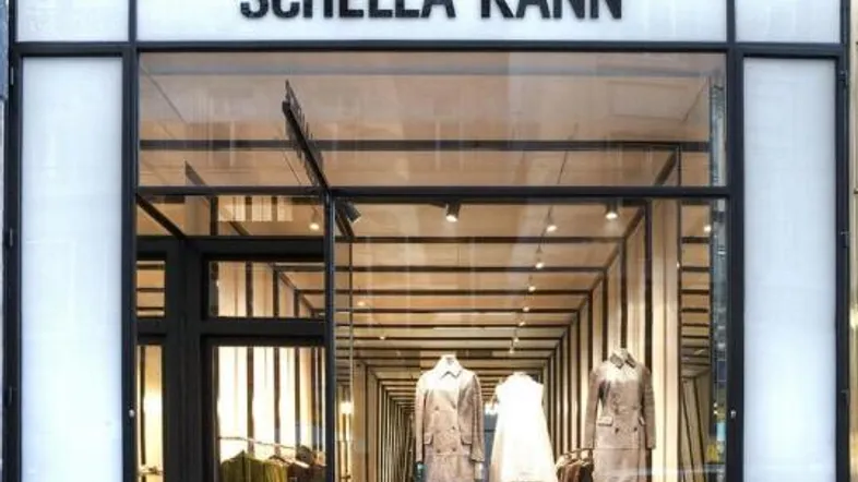 Moderne Ladenfassade mit großen Glasfenstern und Eingangstür, die einen Blick in das Innere des Geschäfts mit Kleidung bietet.