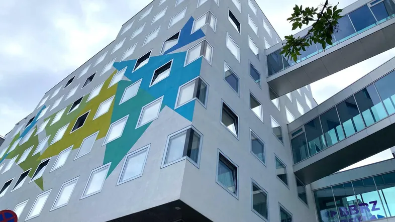 Modernes Gebäude mit farbenfroher geometrischer Fassadengestaltung und gläsernen Verbindungsbrücken unter bewölktem Himmel.