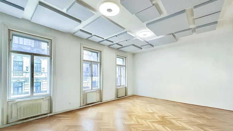 Heller Büroraum mit modernem Schallschutz an der Decke, Fischgrätparkett und hohen Fenstern.